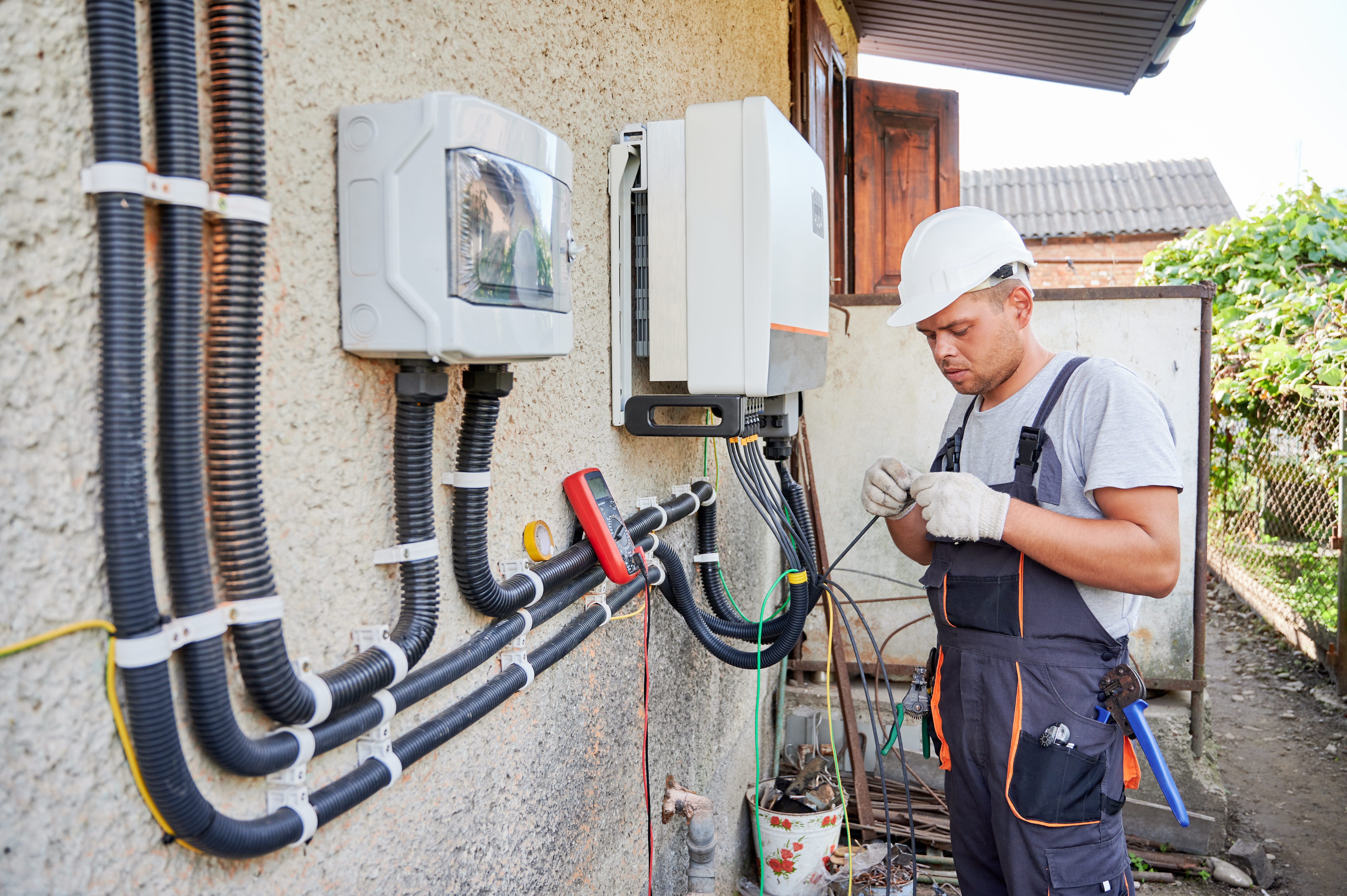 Man electrician installing solar panel system. Technician in helmet and gloves making electrical wiring inverter and electric box. Concept of alternative and renewable energy.