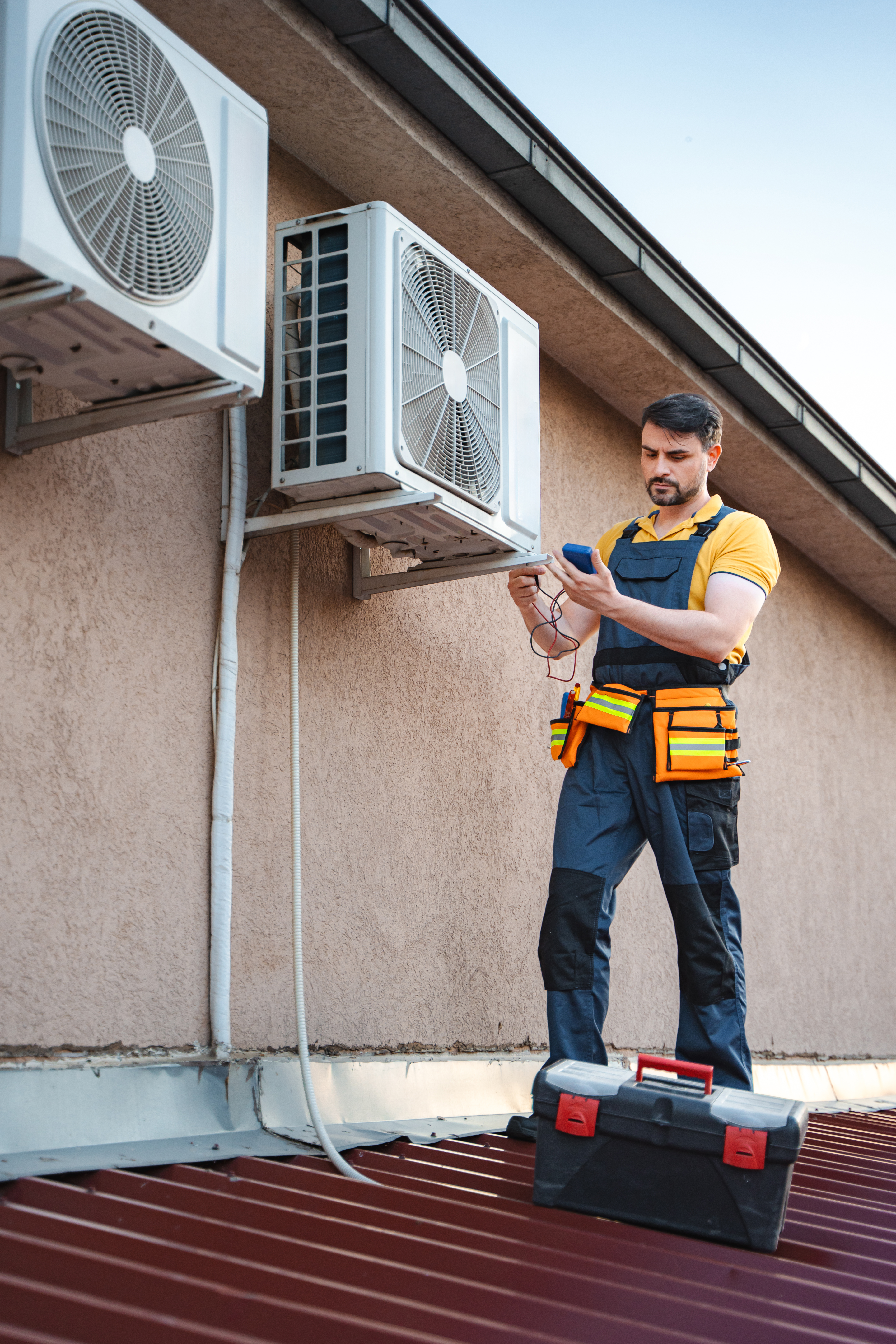 Air conditioner technician installing an air conditioning unit on a roof and checking it with a multimeter