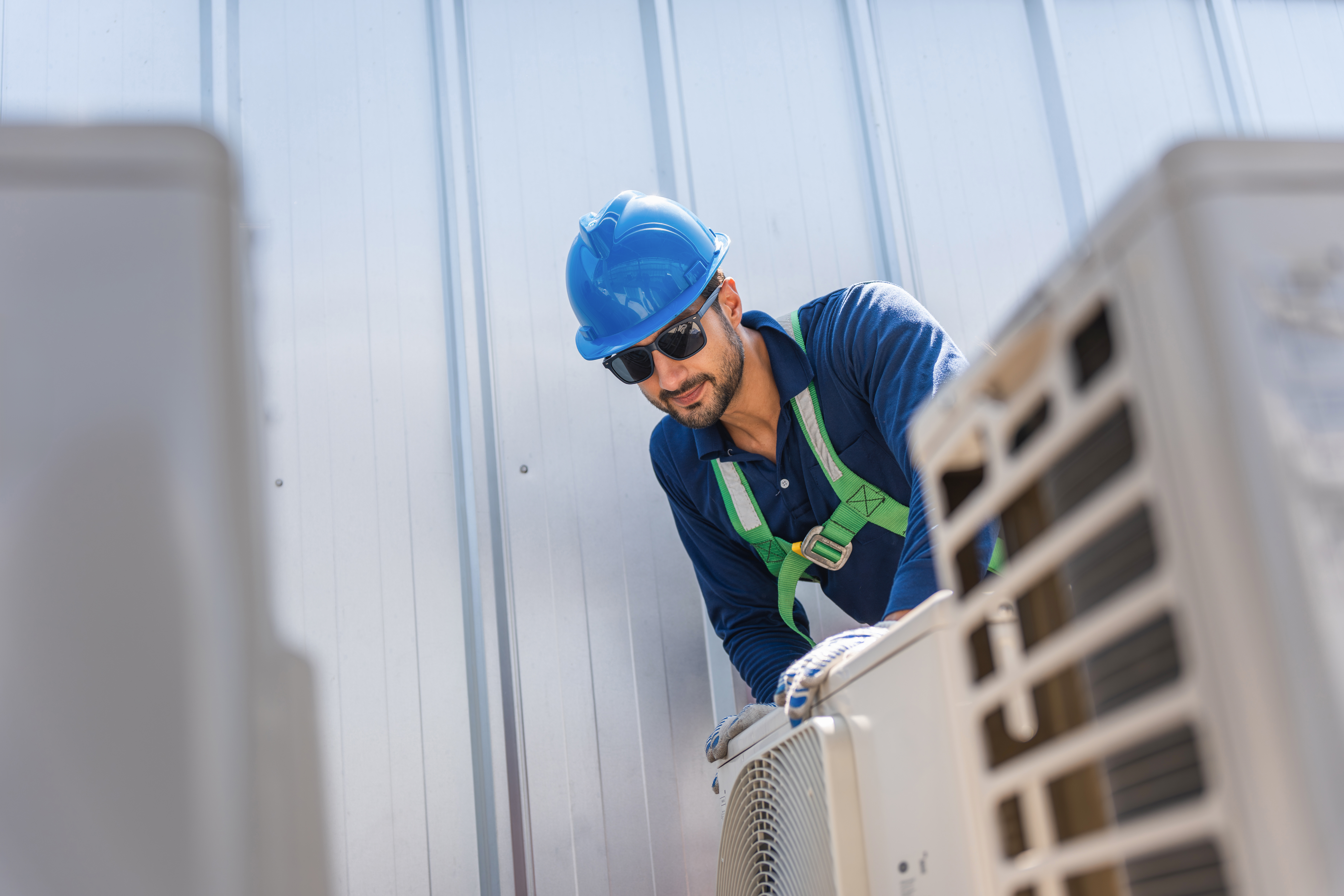Technician in safety gear repairing air conditioning unit on rooftop, HVAC engineer inspecting outdoor condenser system with safety harness, Maintenance worker man service on AC cooling system